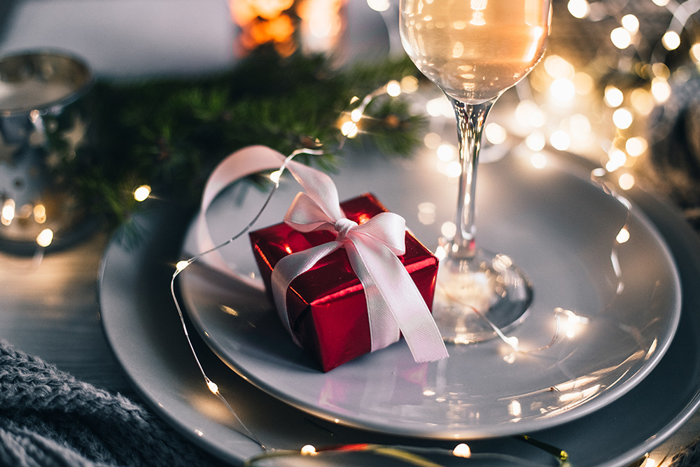Christmas and new year composition gift in a red shiny wrapper on a plate, a glass of champagne, candles and garland