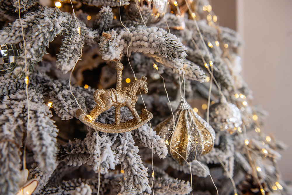 Top view of a snow-covered Christmas tree with trendy toys. New Year festive card with the holidays. Jewelry, toys, gold, silver. Scandinavian fashionable decor style, trendy rustic. Copy space